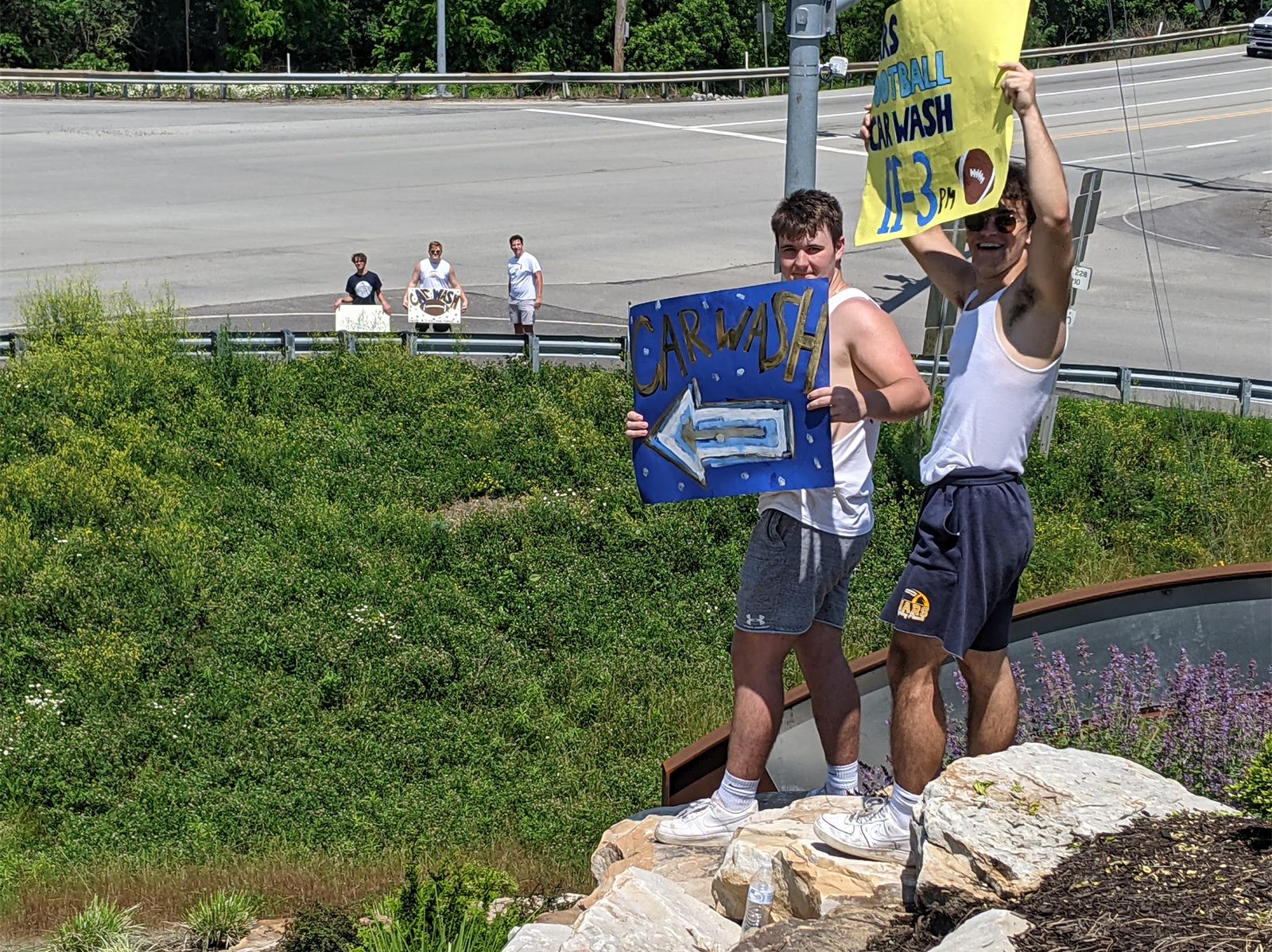 Players holding car wash signs by the road in 2021