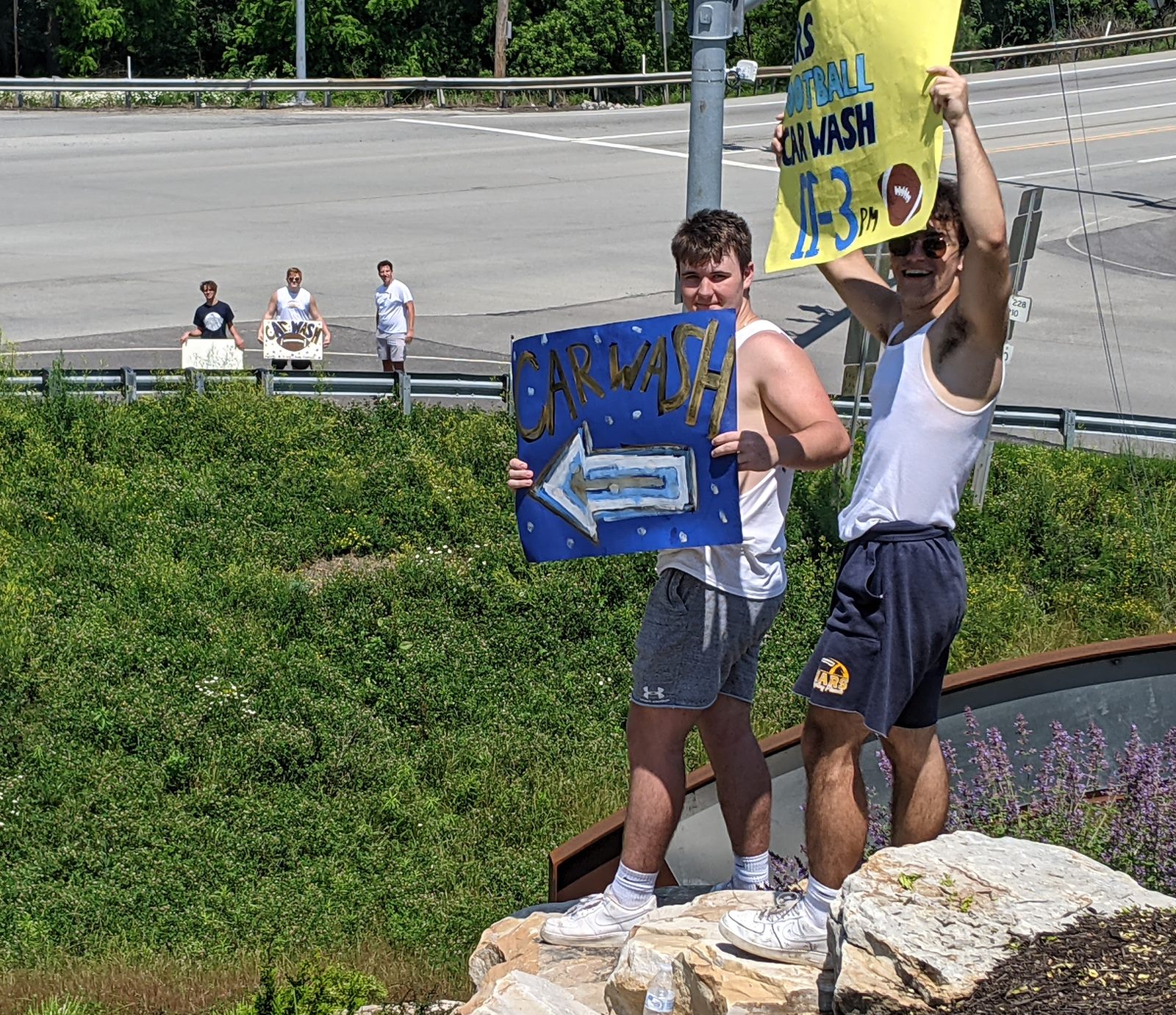 Players holding car wash signs by the road